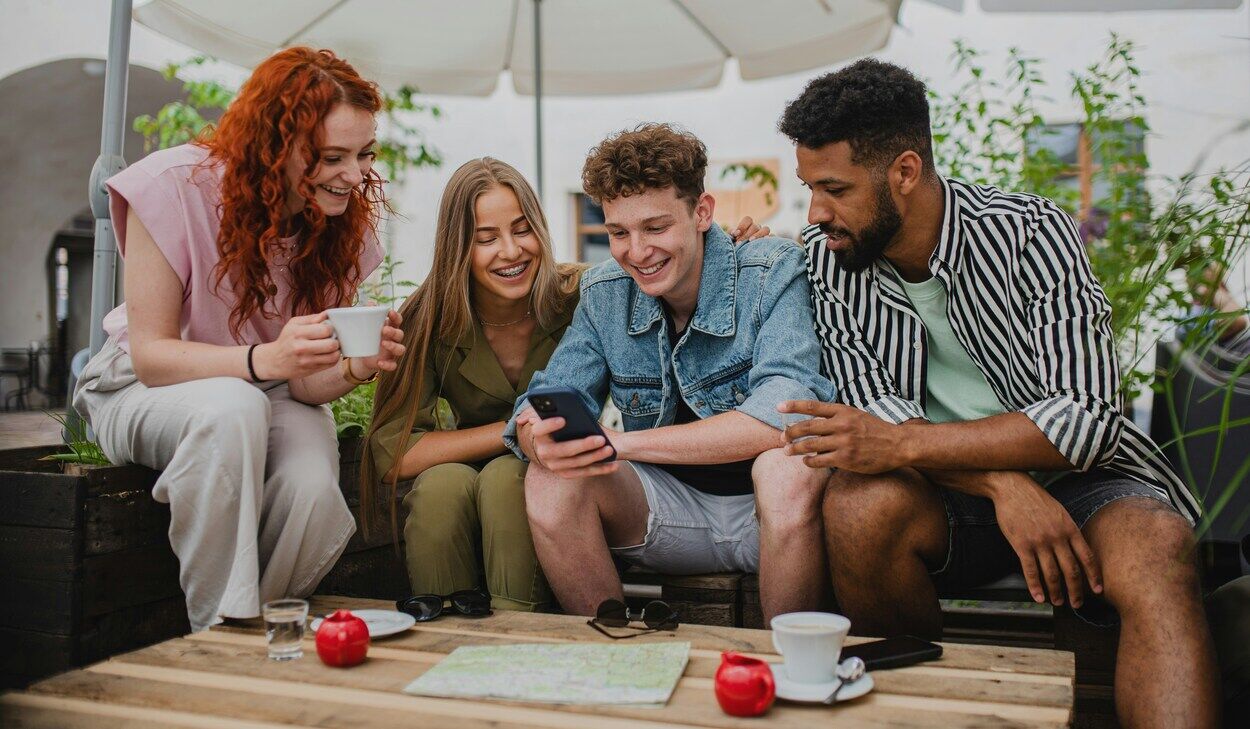 Young friends drinking coffee and laughing while looking at a phone